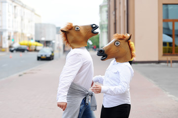 Couple wearing horse masks embrases in city street.