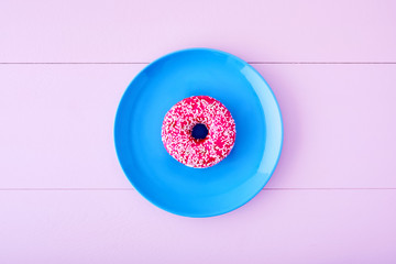 One pink donut or doughnut in a turquois plate on pastel pink wooden table background. Top view.