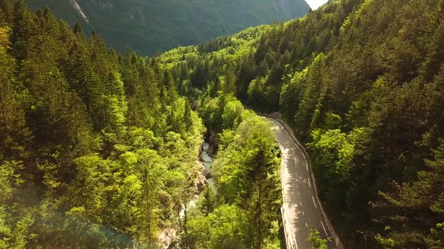 Forward drone shot above a slovenian river flowing in a gorge, next to a road, surrounded by forests