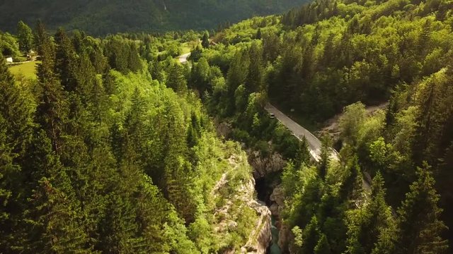 Forward drone shot above a slovenian river flowing in a gorge, next to a road, surrounded by forests