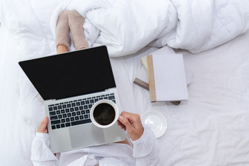 Obraz na płótnie Canvas Close up legs women on white bed in the bedroom. Women working on laptop and drinking coffee in morning relax mood in winter season. Lifestyle Concept.