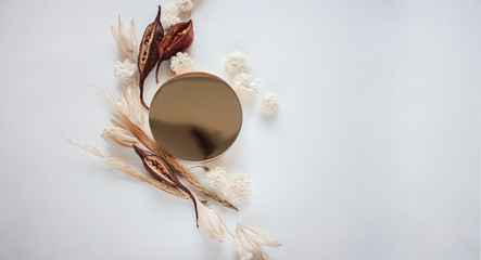 Fototapeta premium Gold jar of cream and dry flowers on white background, top view closeup