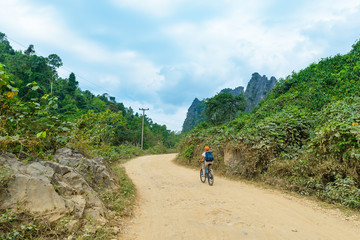 Woman riding mountain bike on dirt road in scenic landscape around Vang Vieng backpacker travel destination in Laos Asia rock pinnacles green valley