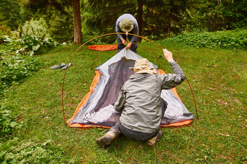 tourism day. tourists - two men in tourist clothes and with special equipment - put up a tent in a...