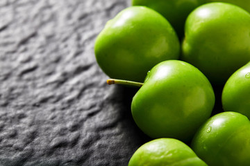 Heap of green gage plum on black textured stone background with copy space. Close up macro view.
