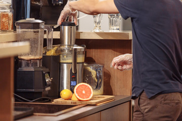 Side view young male bartender makes fruit juice standing behind the bar in the evening bar. Soft drink concept