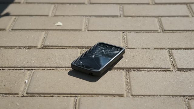 Broken smartphone. A man drops a smartphone on a street tile.