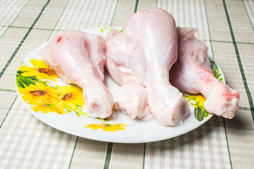 Raw chicken legs on a large plate drain from the water after washing.