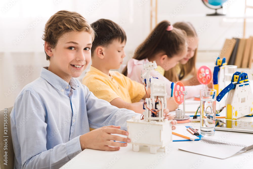 Poster Schoolboy creating robot at lab, smiling to camera