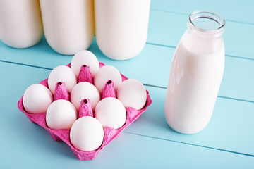 Bottle of milk and white eggs in a pink filler tray on turquoise wooden country kitchen table. Close up ciew from above