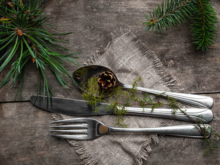 Vintage rustic cutlery set with country style napkin and Christmas decoration - fir tree brunch, cone on wooden background. Copy space, top view.