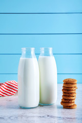 Two bottles of milk and chocolate chip cookies on wooden table with blue wooden background.