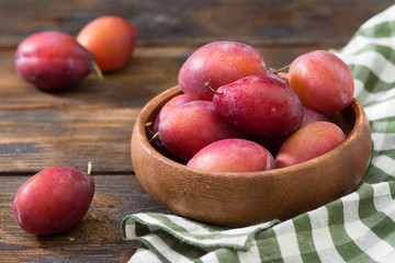 Red plums in a wooden bowl on a wooden table. Rustic style