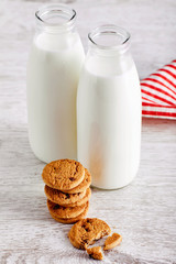 Two bottles of milk and chocolate chip cookies on wooden kitchen table. Close up view from above