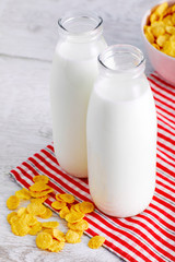 Milk bottles and cereal corn flakes on wooden table. Close up view from above.