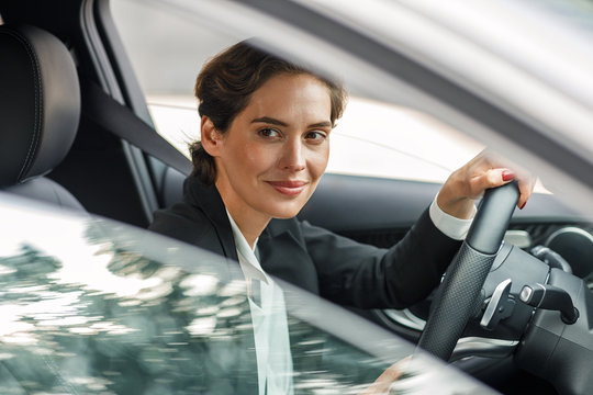 Beautiful Businesswoman In Car Looking Outside A Window. Female In Suit Driving A Car.