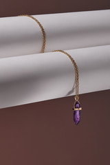 Close-up shot of a golden chainlet with a pendant in the form of screw with a fitted-in violet gemstone similar to a jadeite. The glazy gemstone is elongated and conical.  © RedUmbrella&Donkey