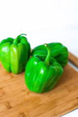 three green pepper large shiny on kitchen Board on white background