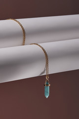Close-up shot of a golden chainlet with a pendant in the form of screw with a fitted-in green-blue gemstone similar to a turquoise. The glazy gemstone is elongated and conical.  © RedUmbrella&Donkey