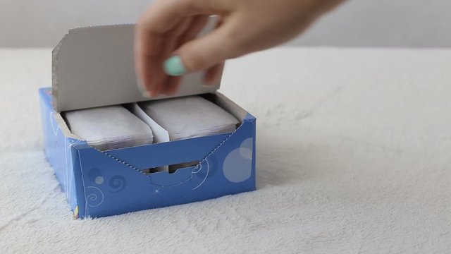 girl opens a box with daily sanitary pads and takes one, close-up, sanitary napkin