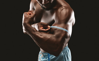 Fototapeta na wymiar Muscular black bodybuilder measuring biceps with tape measure