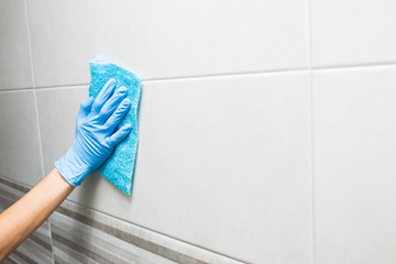 cleaning the toilet room, a hand in a blue glove washes a tile.