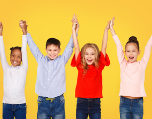 Happy school children raised hands together, yellow background