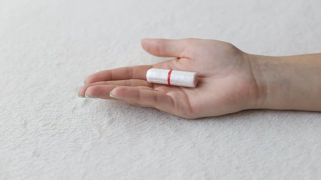 Girl unclenches a fist in which lies a hygienic tampon for menstruation, menstruation concept in girls