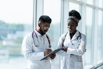 Two doctors: indian male and african female discussing test reports that show on their clipboard