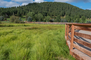 Landscape of wooden walkway, marsh or meadow land and mountains at Dedisse Park in Evergreen, Colorado