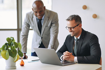 Two smiling businessmen talking together and working with a lapt