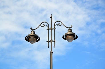 a streetlight pole with 2 lamps in the center over a blue cloudy  sky