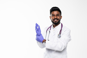 Indian doctor or physician male looking at hand with focused expression as putting on blue surgical latex glove isolated on white background