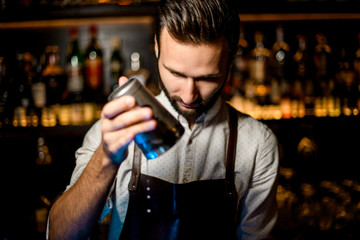 Smiling bartender opening a professional steel shaker making a cocktail