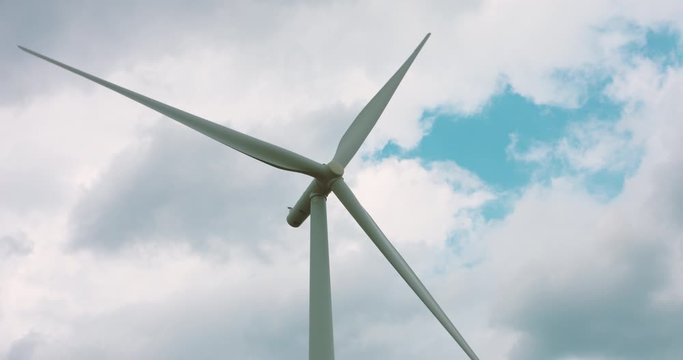 Slow motion wind turbine blades rotating against a cloudy background