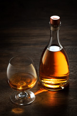 view of glass of  cognac and a bottle aside on color wooden  background. 