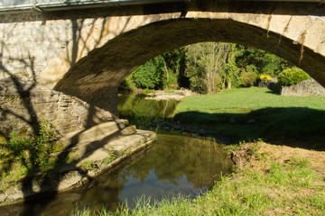 Fototapeta na wymiar Pont en pierre et son arche au dessus d'une rivière pour le passage des vehicules