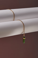 Close-up shot of a golden chainlet with a pendant in the form of screw with a fitted-in green gemstone similar to an axe-stone. The glazy stone is elongated and conical.  © RedUmbrella&Donkey