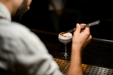 View from above bartender decorated scum of the delicious light violet color cocktail with a yellow flower petals