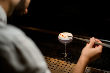 View from above professional bartender decorated scum of the delicious light violet color cocktail with a yellow flower petals