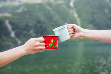 Female hands toasting with cups across. Mint and red cups on nature background. Travel concept, Tatra National park, Poland. Famous lake Morskie Oko © kvitkanastroyu