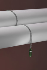 Close-up shot of a steely chainlet with a pendant in the form of screw with a fitted-in green gemstone similar to an axe-stone. The glazy stone is elongated and conical.  © RedUmbrella&Donkey