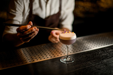 Male bartender decorated scum of the delicious light violet color cocktail with a yellow and purple flower petals