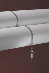 Close-up shot of a steely chainlet with a pendant in the form of screw with a fitted-in lilaceous gemstone similar to an amethyst. The glazy gemstone is elongated and conical.  © RedUmbrella&Donkey