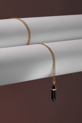 Close-up shot of a golden chainlet with a pendant in the form of screw with a fitted-in dark gemstone similar to a black onyx. The glazy gemstone is elongated and conical.  © RedUmbrella&Donkey