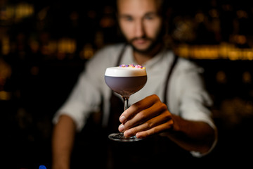 Bartender serving a cocktail with white scum decorated with flower petals in the bar