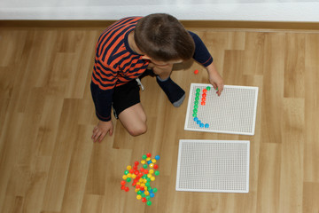 boy, preschooler, collects patterns from colored mosaics, the development of fine motor skills of hands, sitting on the floor, top view, developing concept