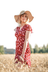 YOUNG AND BEAUTIFUL GIRL IN THE DRESS AND HAT ON THE WHEAT FIELD IN SUMMER