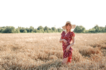 YOUNG AND BEAUTIFUL GIRL IN THE DRESS AND HAT ON THE WHEAT FIELD IN SUMMER