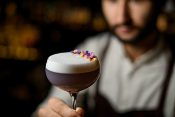 Professional bartender serving a cocktail with white scum decorated with flower petals in the bar